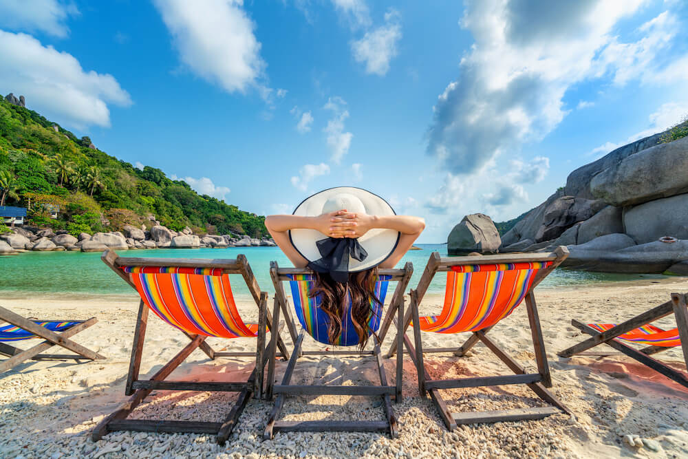 Mujer con sombrero sentada en una silla en una playa tropical